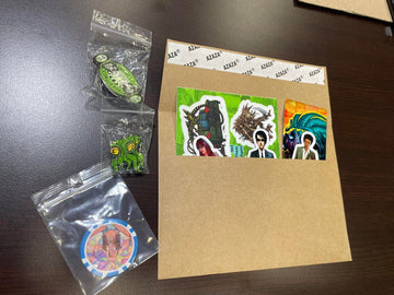Colorful stickers featuring pop culture characters and creatures, arranged in a craft paper envelope on a brown desk.