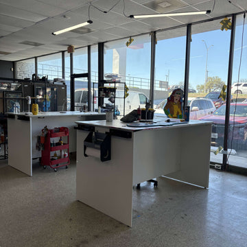Bright workspace with white tables, large windows, and colorful decorations overlooking a parking lot.