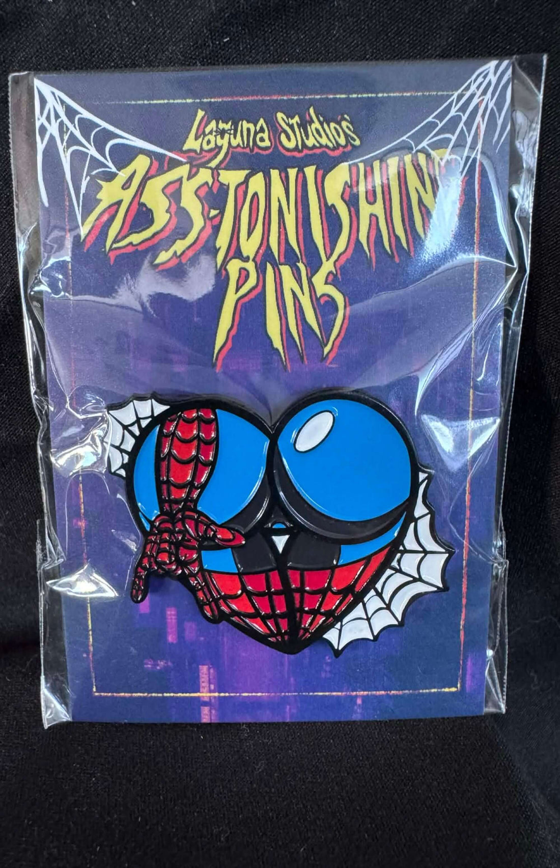 Arachnid ASS-tonishing Pin displayed with packaging from Laguna Studios featuring a comic book design.