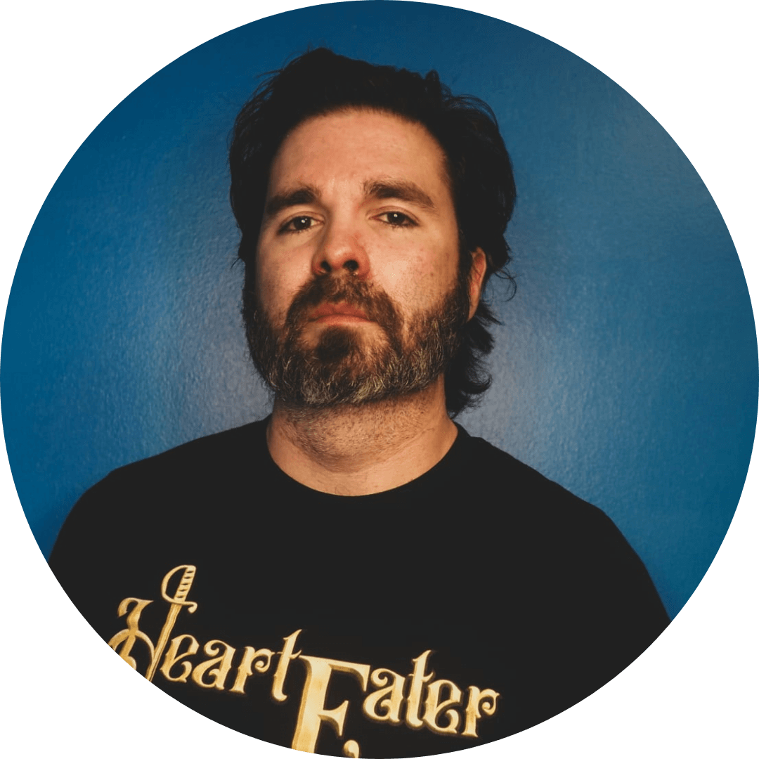 Confident man with a beard in a black Heart Eater t-shirt, posing against a blue background.