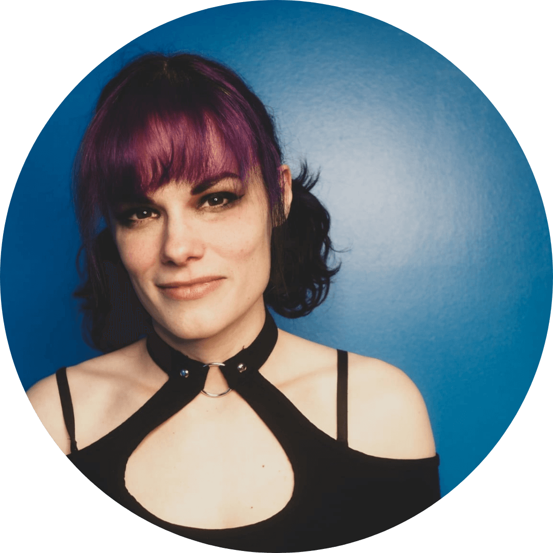 Portrait of a woman with purple hair and stylish attire against a blue background.