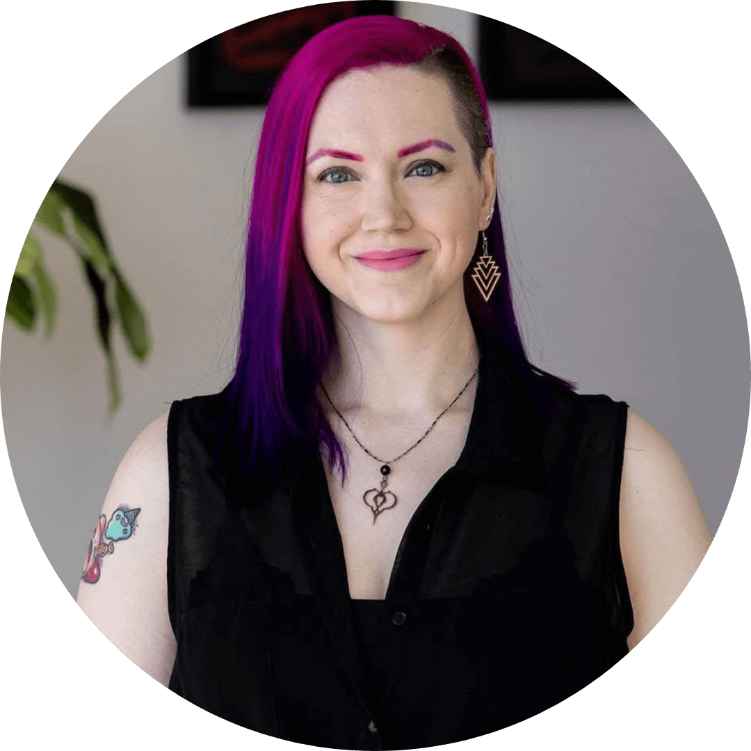 Portrait of a person with vibrant purple hair and tattoos, smiling and wearing stylish earrings.
