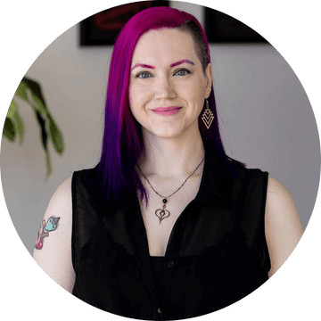 Portrait of a person with vibrant purple hair and tattoos, smiling and wearing stylish earrings.